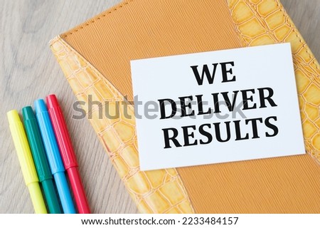 A white business card with we deliver results text on yellow notepad on table, business concept
