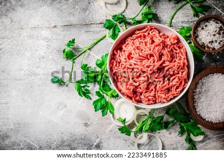 Minced meat in a bowl on a table with parsley and onion rings. On a gray background. High quality photo
