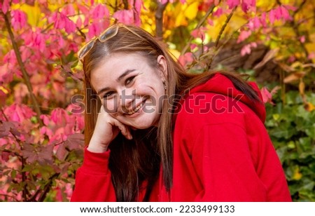 A pretty teen in a red sweatshirt poses on a bright autumn day