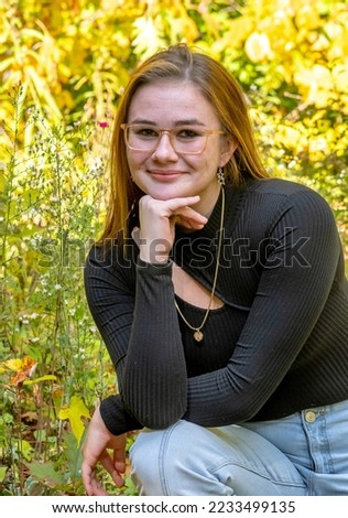 Pretty young lady sits outdoor in a golden and green field, and poses for a senior portrait