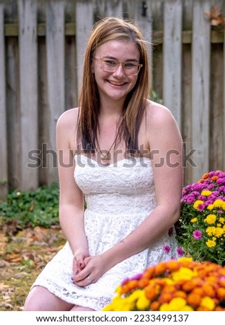 pretty young girl in a sleeveless white dress, poses in a garden with fall chrysanthemums