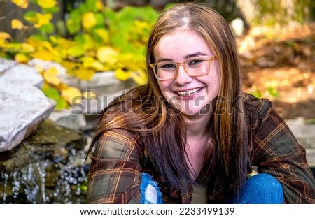Happy girl poses for a senior photo in a flannel shirt and torn jeans