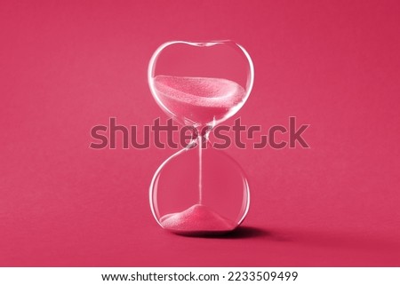 Hourglass, toned monochrome image in Viva Magenta color of the year 2023. Sandglass or sand timer. Single sand clock with golden sand on vibrant paper background. Design element, Royalty-Free Stock Photo #2233509499