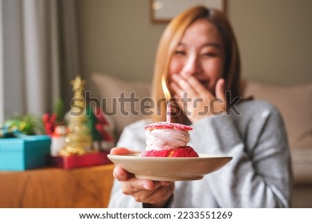 Portrait image of a surprised young woman receiving and holding birthday cake with candle, Christmas holiday decoration at home