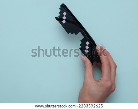 Woman's hand holding pixel glasses on blue background
