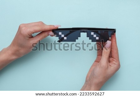 Woman's hand holding pixel glasses on blue background