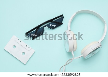 Stereo headphones with Pixelated 8 bit sunglasses and audio cassette on blue pastel background