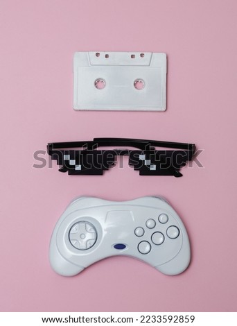 Pixelated 8 bit sunglasses with audio cassette and gamepad on pink pastel background. Top view