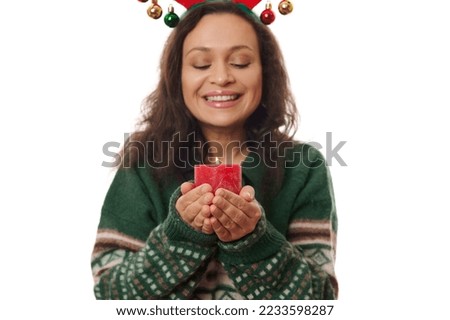 Details: red decorative lit Christmas candle in the hands of a blurred multi-ethnic pretty woman, wearing green warm winter sweater, smiling a beautiful toothy smile, isolated over a white background