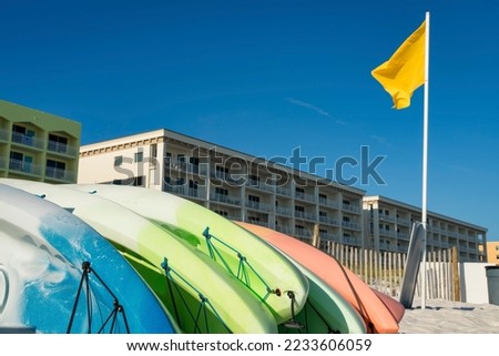 Kayak rentals near the yellow flag on a pole at the front of hotel buildings in Destin, Florida. Kayaks at the front of beachfront hotels against the clear blue sky background.