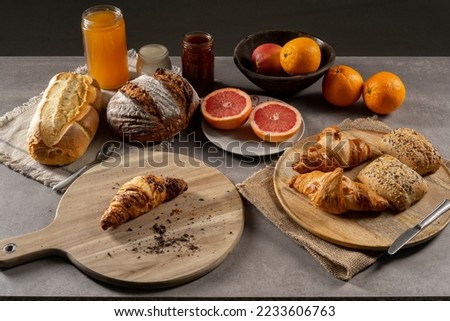 Bread, croissants, rolls, homemade yogurt, marmalade and honey jars, oranges, apples and sliced ​​grapefruit on the table in a rustic wooden bowl and wooden plate