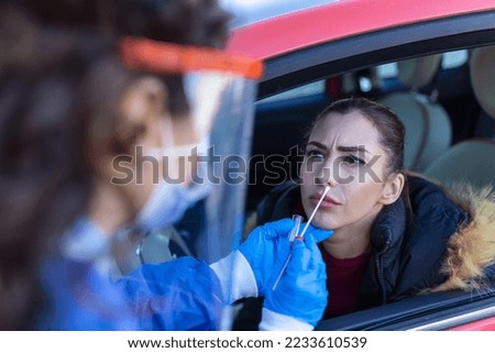 Woman getting tested at a coronavirus drive thru station by medical staff with PPE suit by throat swab. Health care drive thru service and medical concept