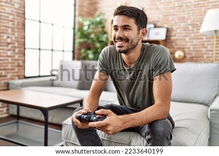 Young hispanic man smiling confident playing video game at home