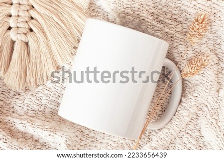 Mockup of white mug on knitted plaid with macrame decor and dried flowers, neutral color. Blank coffee cup mug mock up in Boho style, flat lay.