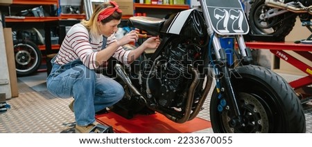 Mechanic woman with screwdriver repairing custom motorcycle over platform on factory