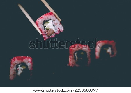 Female hand takes california sushi rolls with Chinese chopsticks. Selective focus, black background.