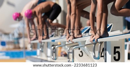 Teenage children on the starting blocks ready to dive into the pool at the beginning of a swimming race