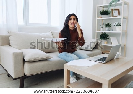 A woman freelancer is rude and talks on the phone with anger from working with documents in her hands looking at her laptop on her desk in her home office