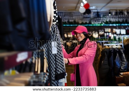 Pretty young woman buyer choosing clothes from rack in clothing store