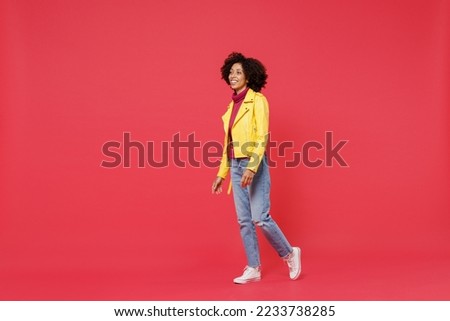 Full size body length bright fascinating happy fun bright young curly black latin woman 20s years old wears yellow jacket go move stroll looking aside isolated on plain red background studio portrait Royalty-Free Stock Photo #2233738285