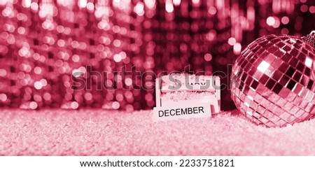 Silver glass disco ball. New Year's background with blurred bokeh, on the wooden block December. Selective focusing and shallow depth of field. Viva Magenta toned. Trendy color 2023