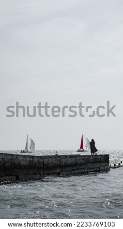 The girl on the shore of the cold sea looks at the yachts