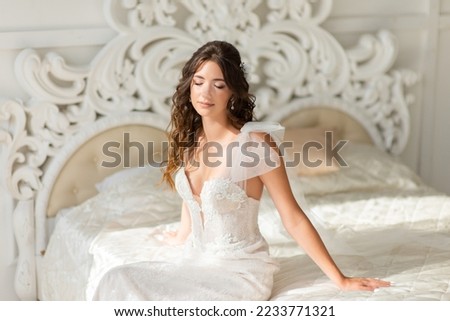 Woman in a wedding dress with a beautiful hairstyle, on a white bed in the studio