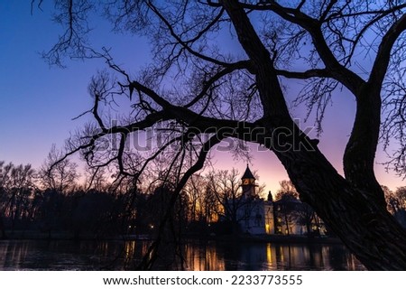 Colorful dramatic sky during sunset over the trees in the palace park. Dark outlines of trees on the near horizon. Contours of the palace in the distance