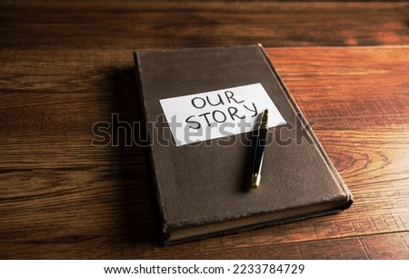 On the cover of the book is paper with the inscription Our story. On a wooden table Royalty-Free Stock Photo #2233784729