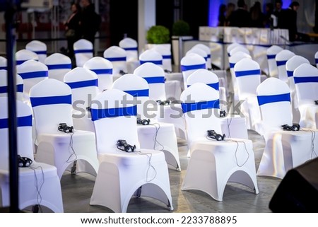 Banquet event chair with white spandex covering, blue strap, sash interpreter receiving device tight fitting Royalty-Free Stock Photo #2233788895