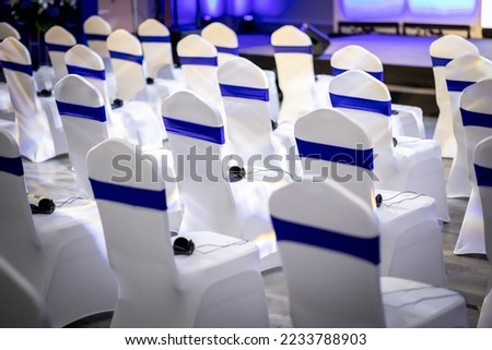Banquet event chair with white spandex covering, blue strap, sash interpreter receiving device tight fitting Royalty-Free Stock Photo #2233788903