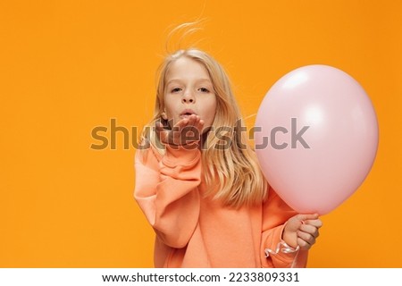 beautiful cute girl in orange clothes on an orange background stands with a pink balloon in her hand and sends an air kiss
