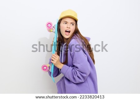 an emotional woman stands half sideways on a white background in a purple suit and a yellow cap, discontentedly clutching a skate holding it with both hands