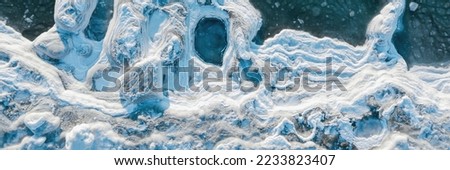 Top view of the icy seashore. Winter aerial photograph of the sea coast. Ice floes and freezing sea water. Nature of the Extreme North. Cold winter weather. Harsh arctic climate. Natural background.