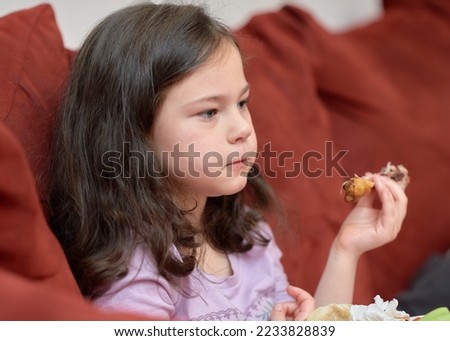expressive young girl is eating chicken and vegetables for dinner on the couch while watching TV