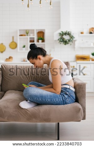 Young woman holds a smartphone in her hands, hunched over sitting on the couch Royalty-Free Stock Photo #2233840703