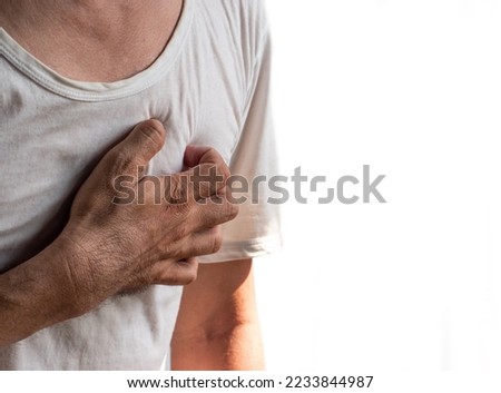 Asian young man suffering from left sided chest pain. Chest pain can be caused by heart attack, myocardial infarct or ischemia, myocarditis, pneumonia, stress, etc. Royalty-Free Stock Photo #2233844987