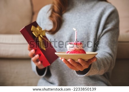 Closeup image of a woman holding a gift box and birthday cake with candle