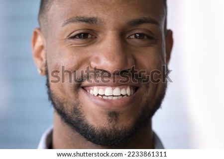 Happy attractive young African guy face close up portrait. Handsome Black man looking at camera with toothy smile, showing healthy white perfect teeth, promoting dental service, male beauty care