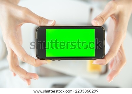 closeup hand holding smartphone top view in restaurant with blank space green screen colored 
