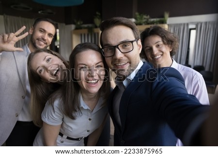 Five happy business people in formal wear making selfie picture, holding device, smiling faces looking at smartphone screen pose together in office, use modern tech, having fun, showing companionship
