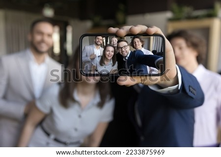 Close up on cellphone screen view of group of happy business people holding smartphone looking at device screen make selfie picture having fun during break at workplace. Friendship, modern tech, apps