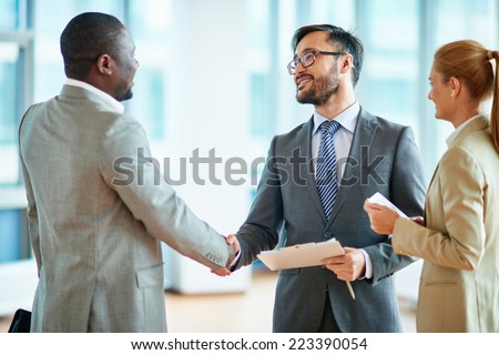 Two businessmen making agreement, their female colleague standing near by