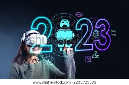 Businesswoman in casual wear wearing headset watching at metaverse reality with vr equipment. Dark background with 2023 neon sign, virtual globes. Concept of modern technology and progress in business