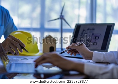 Professional design engineers discuss calculations to use pure natural energy and installing solar panels and wind turbines on the roof of houses to generate electricity, energy saving and global warm Royalty-Free Stock Photo #2233929877