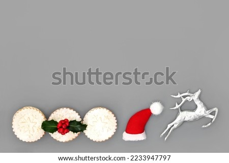 Christmas holiday background with traditional festive symbols of reindeer, santa hat and mince pies on grey background. Abstract minimal design for Xmas and New Year holiday season.