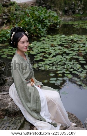 Full length portrait of a very beautiful Asian lady in vintage dress sitting by a pond in a traditional China garden looks like a fairy. Vintage portrait is popular in China, Asia. 