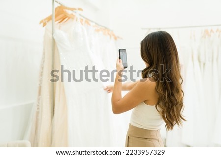 Rear view of a future bride taking pictures photos with her phone at a beautiful wedding dress