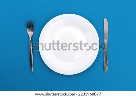 On a blue background is a plate with a fork and a knife. Royalty-Free Stock Photo #2233968077