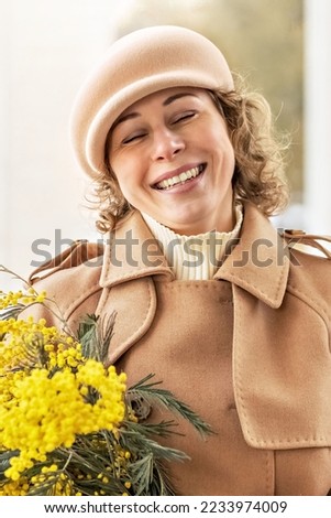 Portrait of a young woman in a beige coat and hat with a bouquet of mimosa in her hands. Spring, International Women's Day March 8.